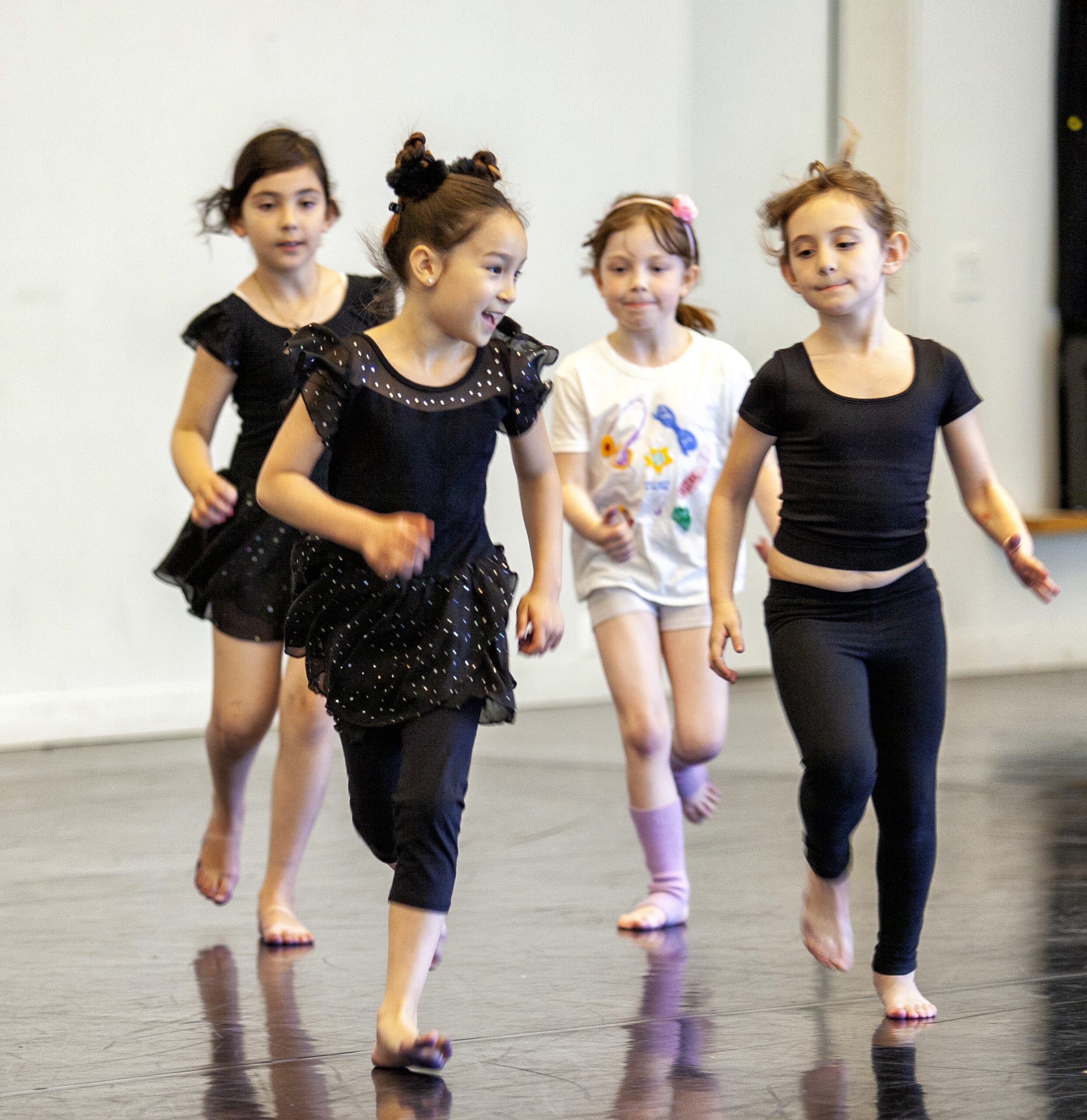 Four young dancers running across a dance studio during a Taylor School movement class